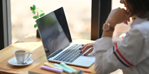 Cropped shot woman using/typing on computer laptop that putting on wooden working desk with coffee...