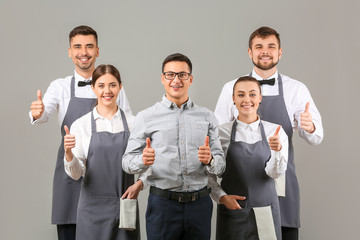 Group of waiters with teacher showing thumb-up on grey background