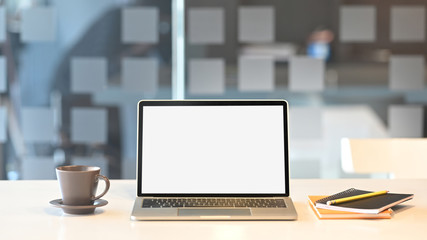 Fototapeta premium Computer laptop with white blank screen putting on wooden table with coffee cup and notebook over orderly living room as background.