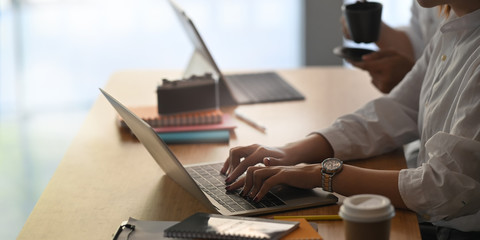 Closeup website administrator team working with computer tablet and laptop while sitting together at the modern wooden table over luxury cafe as background. Working outside the office concept.