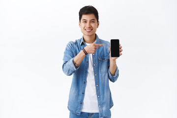 Technology, online lifestyle concept. Portrait of charismatic asian guy introduce application, showing you profile of girl likes, pointing smartphone screen, recommend dating app, white background