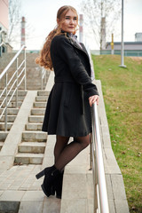 Photo of a fashionable blonde girl in a coat on the stairs outdoors in the spring city