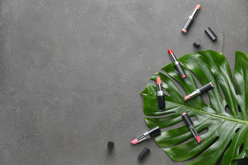 Different lipsticks and tropical leaf on grey background