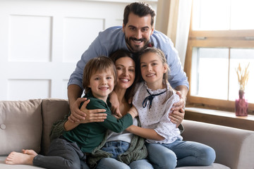 Happy young bearded man cuddling sitting on cozy couch beautiful wife with small daughter and son....