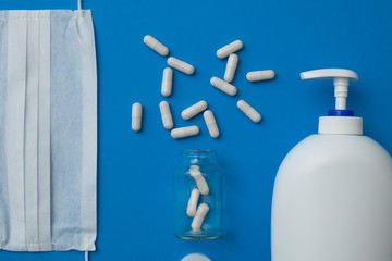 facial disposable medical mask, white pills and liquid hand soap isolated on blue background.