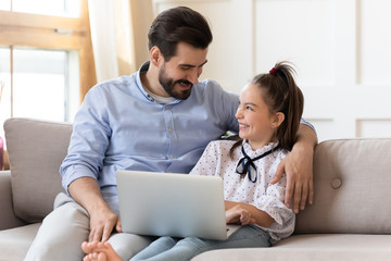 Smiling dad hugging little daughter, laughing at comedy movie or funny cartoons at home. Loving...