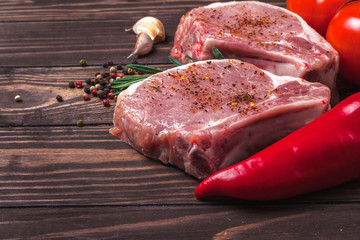 Pork steak with spices, vegetables and rosemary. Juicy and fresh raw meat, tomatoes, paprika, henna, and peppercorns on a wooden tabletop