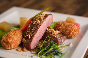 Roasted duck breast steak with potato croquettes, baby carrot, pear cubes on a white plate