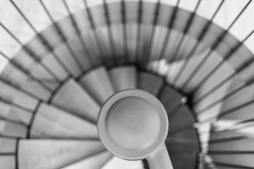 Spiral staircase, forged handrail and wooden steps in modern home. In the foreground is a railing. The view from the top.