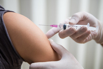 Vaccine or flu shot in injection needle. Doctor working with patient`s arm
