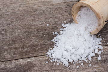 Closeup natural sea salt in wooden bucket splashing on old rustic wood table background. 
