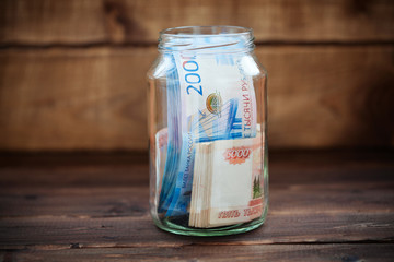 Money in a glass jar on a wooden background. Russian banknotes. 