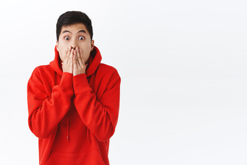 Waist-up portrait of shocked speechless asian man, gasping, cover mouth and stare camera, express shook with eyes, gossipping, heard exciting incredible news, cant believe, white background