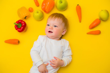 Fototapeta na wymiar Healthy child nutrition, food background, top view. Smiling baby 8 months old surrounded with different fresh fruits and vegetables on yellow background. Baby first solid feeding.baby with vegetables