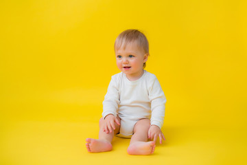 Healthy baby in white bodysuit sits on a yellow background, space for text