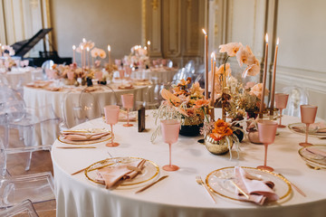 banquet tables with white tablecloths are in the hall of the old house, on the tables are flower arrangements, candles, plates with napkins, glasses and cutlery