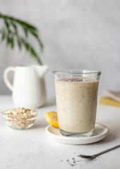 Delicious banana smoothie with oatmeal, coconut milk and chia seeds. healthy breakfast, snack. monochrome. gray background with green leaves. vertical image. selective focus.