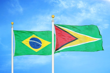 Brazil and Guyana two flags on flagpoles and blue cloudy sky