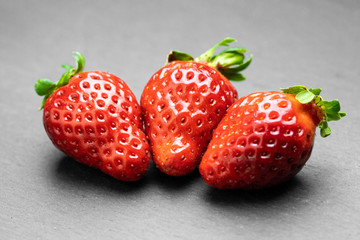 Three juicy strawberries lying on a dark surface
