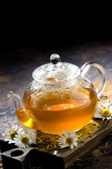 glass teapot of chamomile tea on dark background, vertical