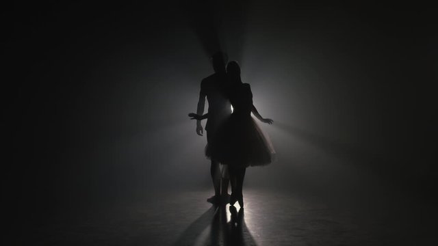 Romantic professional ballet pair practicing moves on dark stage. Young couple dancing in classic dress, spinning around and smiling. Gracefulness and tenderness in every movement.