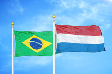 Brazil and Netherlands two flags on flagpoles and blue cloudy sky