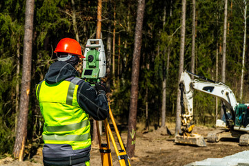 Surveyor engineer with equipment (theodolite or total positioning station) on the construction site of the road or building with construction machinery background