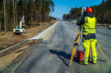 Surveyor engineer with equipment (theodolite or total positioning station) on the construction site of the road or building with construction machinery background