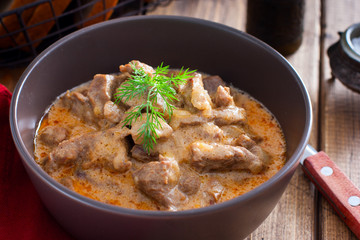 Traditional beef stroganoff in a ceramic bowl on a wooden table, selective focus