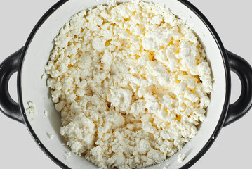 White cottage cheese in a black bowl. lots of cheese on a white background.