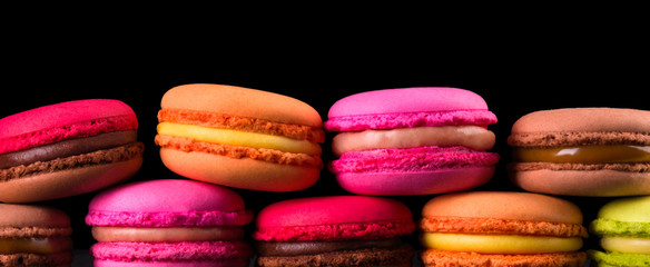Stack of french colorful macaroons in row isolated on black background