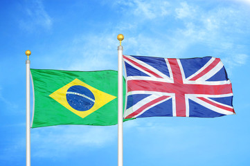 Brazil and United Kingdom two flags on flagpoles and blue cloudy sky