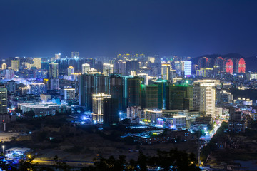 Obraz premium Night view of Sanya city with bright multi-colored illumination buildings, structures, roads, sidewalks, poles, bridges.
