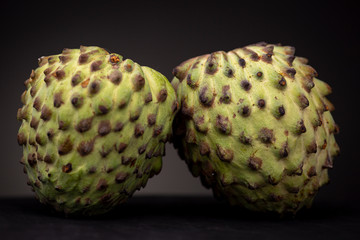 Close up of two Soursop or Graviola fruit related to the Sugar Apple with prickly vibrant green peel. Low key studio shot of fresh food.