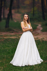 Obraz na płótnie Canvas bride in wedding dress crossed her arms and smiles. walk in the