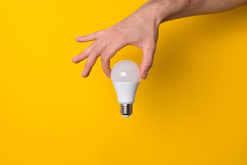 close up man hand holding white led light bulb against yellow background. concept of creativity,...