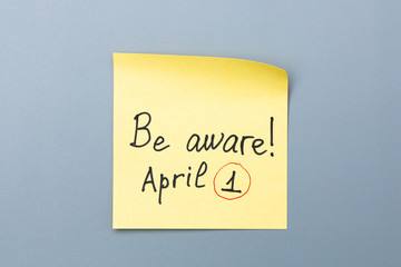 be aware on yellow sticky note over a grey background. april fools day