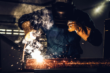 Metal welder working with arc welding machine to weld steel at factory while wearing safety...