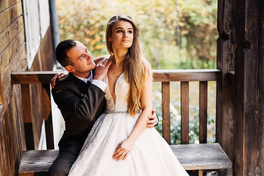bride in wedding dress sits with groom in uniform on bench near