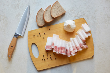 Top view of knife and slices of bread near cutting board, having lard an garlic to taste, Ukrainian traditional appetizer, food composition, eating habits, lunchtime. People and traditions concept.