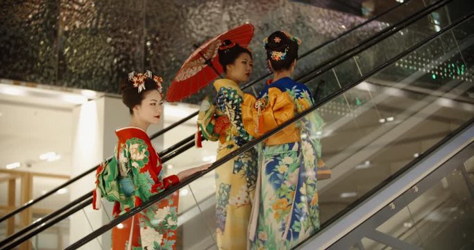 Three beautful japanese geishas in traditional kimono dresses walking in shopping cenre, standing in escalator and chatting - traditional culture in modern japan 4k footage