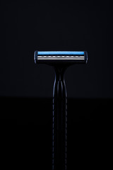 Disposable shaving machine. Black razor on a black background. Black razor with a blue line.