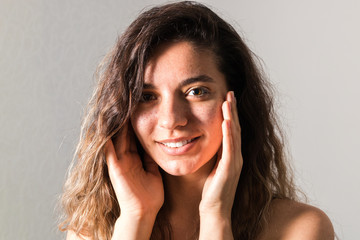 portrait of tender young woman with curly hairs smiling and touching her face against blue background