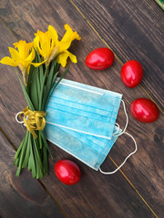 Easter red eggs, medical masks from coronavirus, a cup of tea on a vintage table, yellow daffodils, white crocheted napkin. Background, wallpaper or postcard.