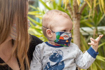 Portrait of baby and mother together with homemade reusable protective face mask against...