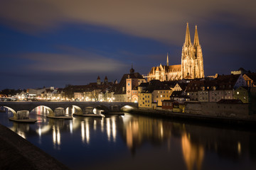 Fototapeta na wymiar Illuminated saint Peter cathedral with historical stone bridge after dark in Regensburg, Bavaria, Germany. Cityscape image over the Danube river from Sorat Hotel terrace.