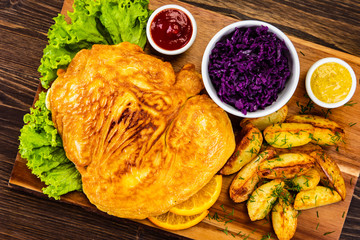 Schnitzel with baked potatoes on wooden background