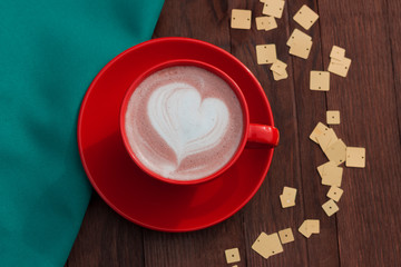 Red cup of cacao on wooden background with green textile and yellow sequins.