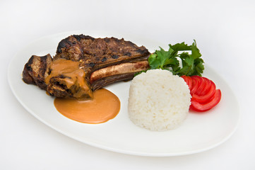 T-bone pork meat, rice, tomatoes, parsley and meat sauce on a white plate on a white plate