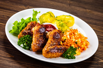 Fried chicken wings with boiled potatoes and vegetable salad on wooden board